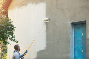 a person painting the exterior of a house using a paint roller